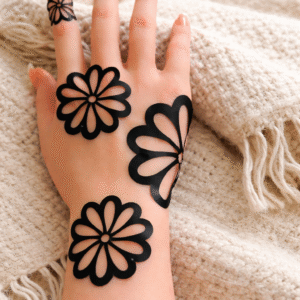 Black floral henna design applied on the back of a woman's hand resting on a soft beige knitted blanket.