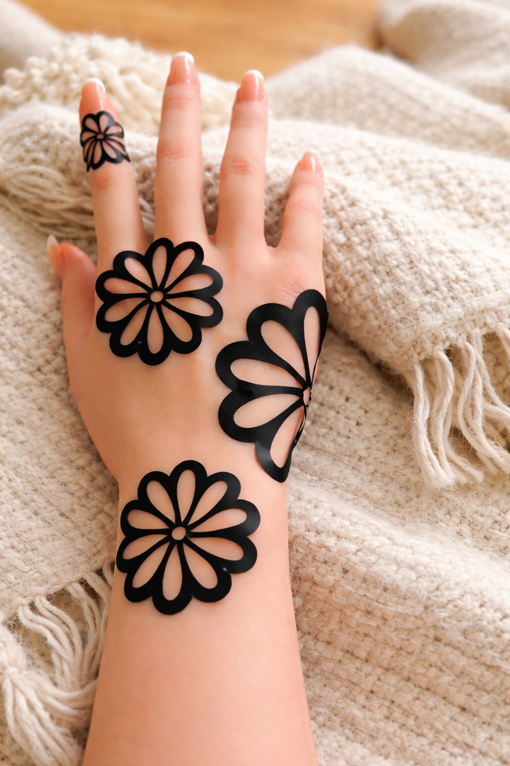 Black floral henna design applied on the back of a woman's hand resting on a soft beige knitted blanket.