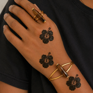 Woman wearing black clothing with Hibiscus floral henna designs on the back of her hand and forearm, paired with gold rings and bracelets.