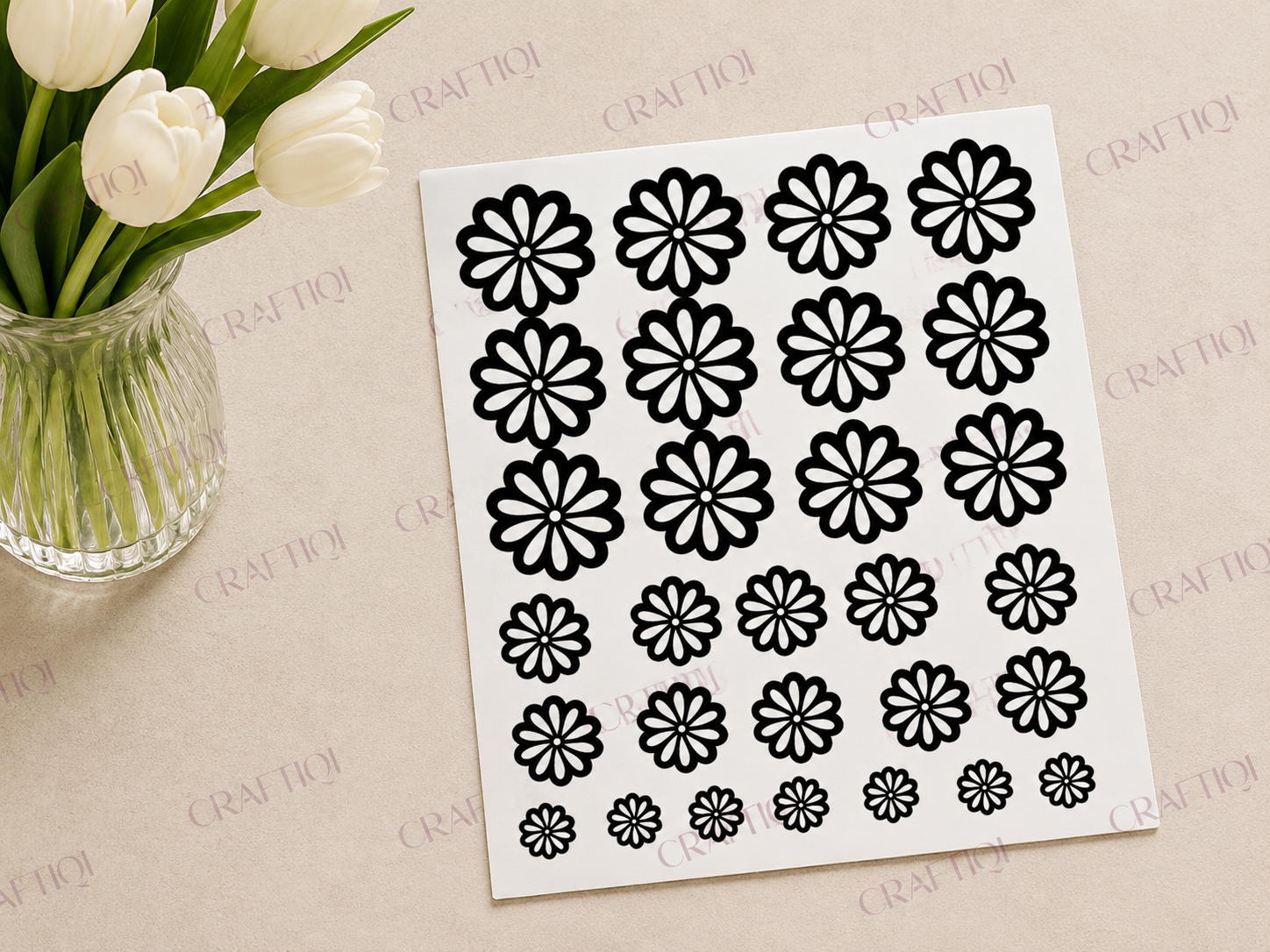 Black floral sticker sheet with daisy designs in multiple sizes displayed at an angle on a soft beige background with white tulips and a subtle Craftiqi watermark.