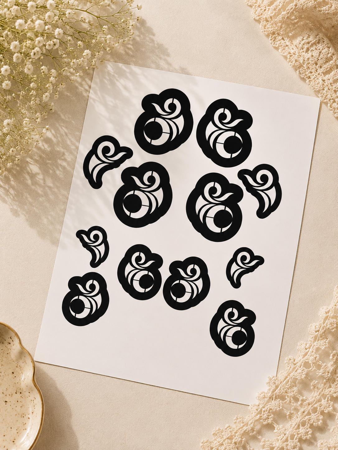 A4 henna stencil sheet with circular swirl designs in multiple sizes displayed at an angle on a soft beige background with delicate white flowers and lace accents.